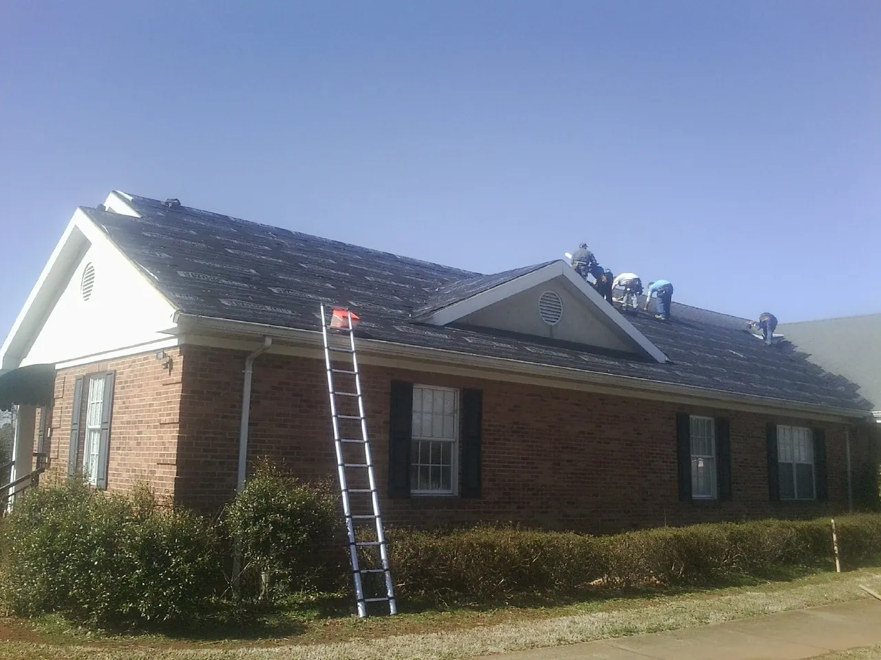Crew tearing shingles off a brick ranch roof with a ladder set — Emergency Roof Repair work by our crew in Orleans