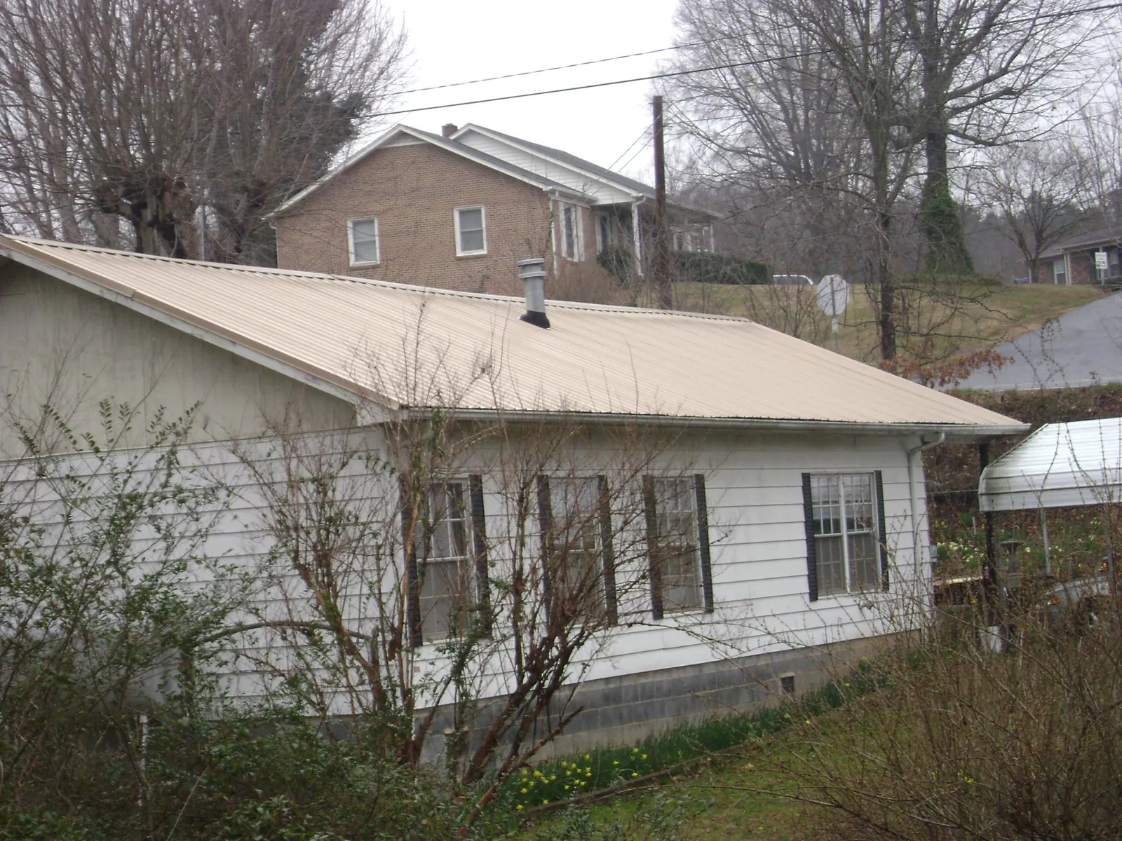 Tan metal roof on a white sided house set into a hillside — Commercial Roofing by Roofing Brothers in Orleans